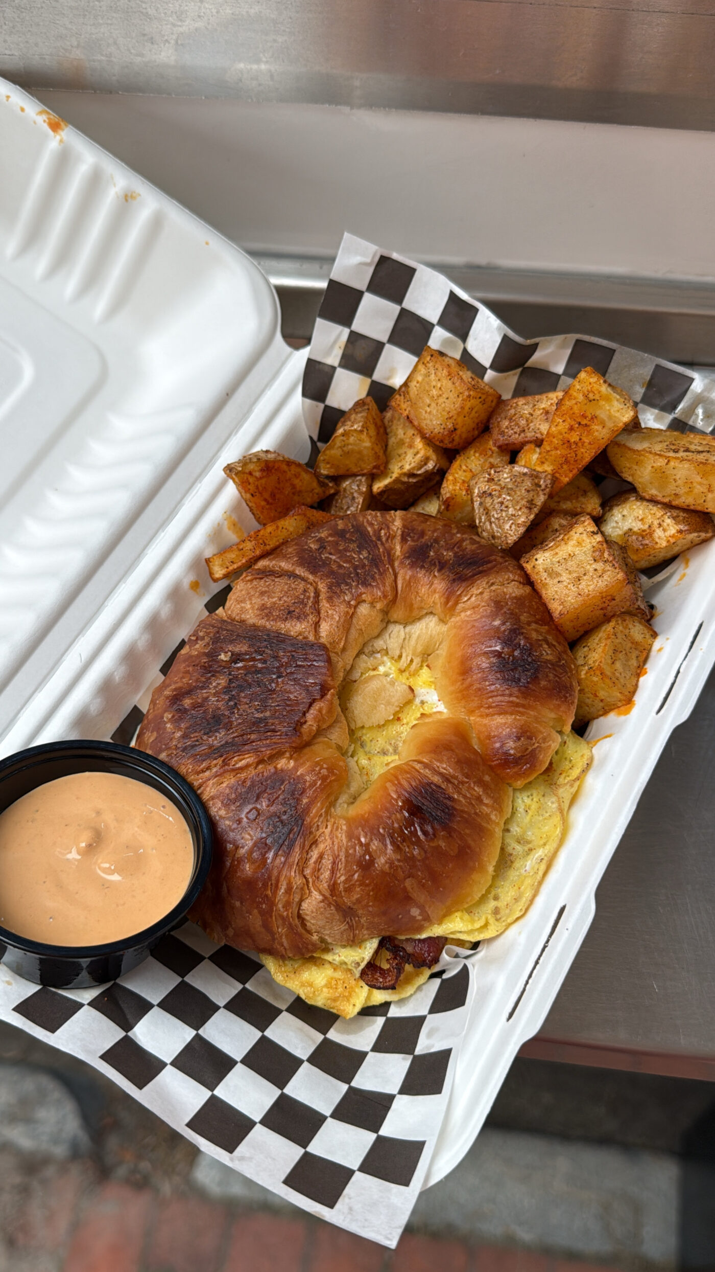 Croissant breakfast sandwich with egg and bacon, served with home fries and chipotle crema